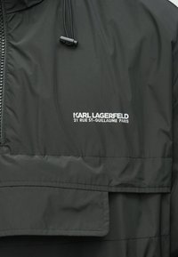Μαύρο μπουφάν με φερμουάρ και κορδόνι, λευκή επιγραφή "KARL LAGERFELD 21 RUE ST-GUILLAUME PARIS" στο μπροστινό μέρος.
