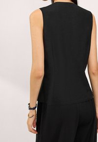 Top senza maniche nero con una silhouette aderente e una texture liscia, caratterizzato da un collo alto e una lunghezza che arriva ai fianchi.