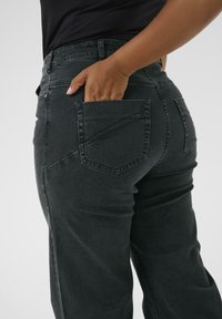 Dark gray jeans with a fitted design, featuring a back pocket and subtle stitching details. The fabric appears sturdy with a slight texture.