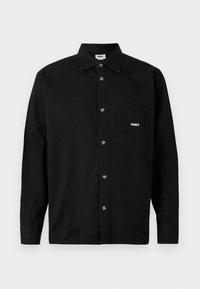 Camisa preta de botões feita de algodão com gola, apresentando botões em tom dourado e um bolso no peito esquerdo com o logótipo branco "OBEY".