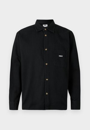 Sort skjorte med knapper lavet af bomuld, med krave, der har guldfarvede knapper og en venstre brystlomme med hvid "OBEY" logo.