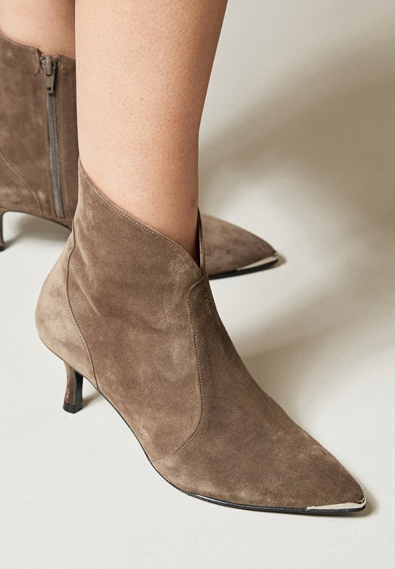 Botine din suede maro, cu vârf ascuțit, toc mic și închidere cu fermoar în spate. Prezintă o textură netedă, elegantă și un design rafinat.