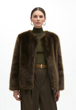 Chaqueta de pelaje sintético marrón con un silueta corta, cuello redondo y textura suave; combinada con una blusa verde de cuello alto y un cinturón marrón.