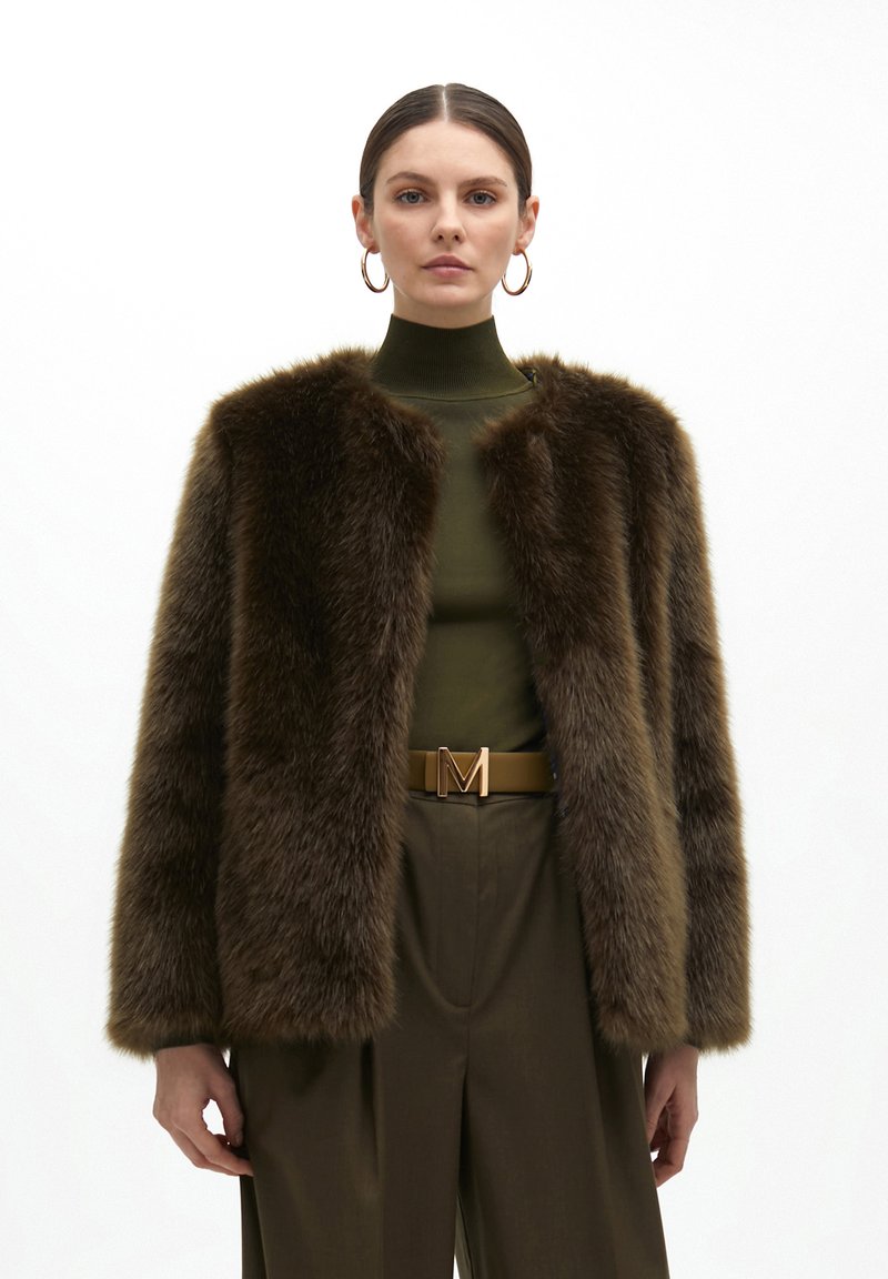 Brown faux fur jacket with a cropped silhouette, rounded neckline, and soft texture; paired with a green high-neck top and brown belt.