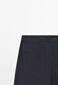 Donkerblauwe op maat gemaakte broeken met een gladde textuur, voorzien van riemlussen en twee achterzakken met horizontale openingen.