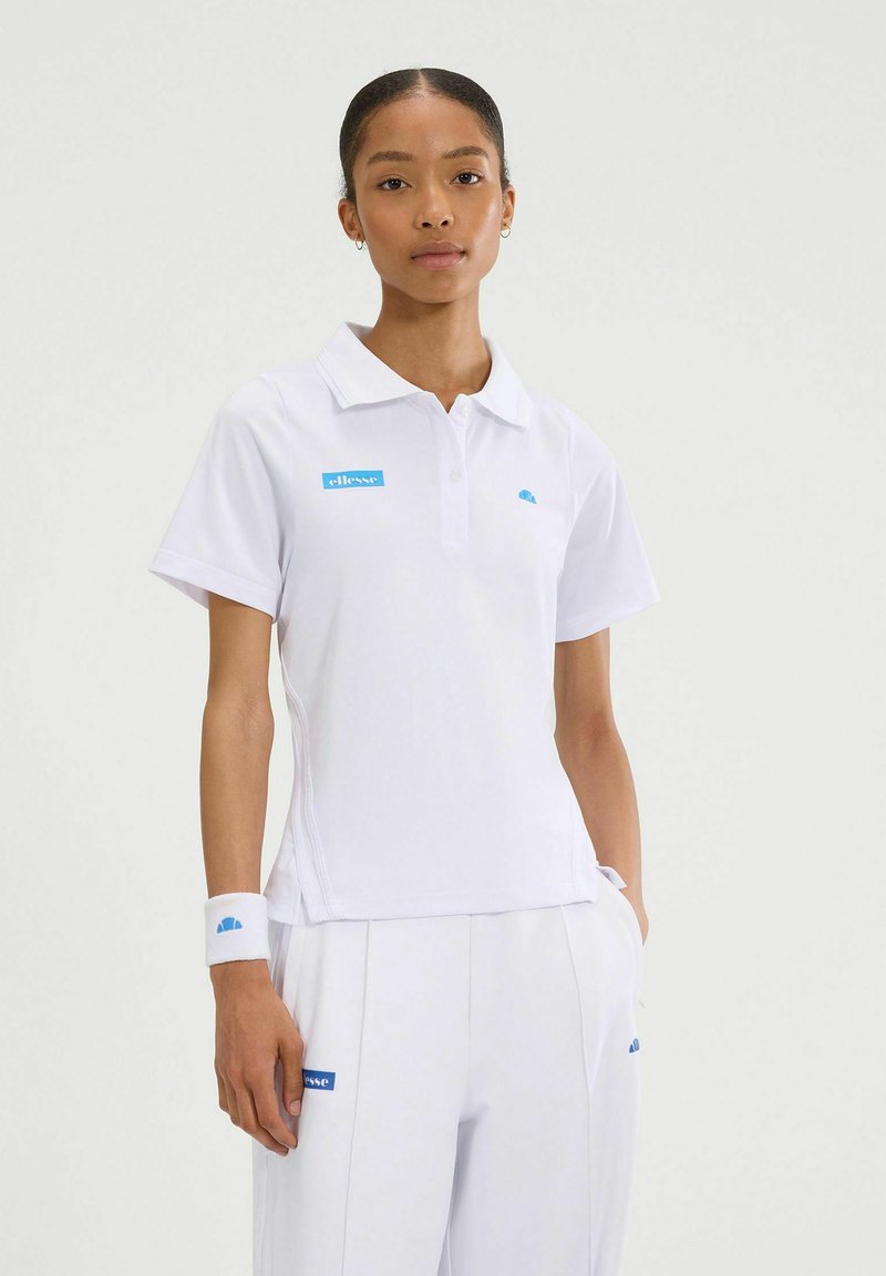 Camisa polo blanca de manga corta, con un logotipo y acentos en azul claro. El material parece suave; combinada con pantalones blancos y una pulsera.