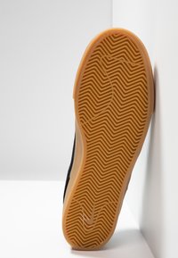 Sneaker nera con una tomaia nera a trama, caratterizzata da una suola in gomma marrone chiaro con motivo a spina di pesce e un dettaglio del logo.