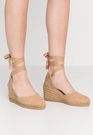 Beżowe sandały na koturnie espadryle z tkaniny, z owrapowanymi sznurkami na kostce i plecionym detalem z juty na obcasie, ukazujące fakturowane powierzchnie.