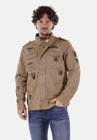 Giacca militare color khaki con numerosi ricami, colletto strutturato, chiusura con bottoni e quattro tasche frontali; realizzata in un tessuto resistente.