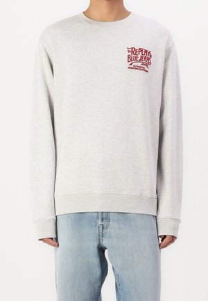 Lysegrå langærmet sweatshirt med rødt "Replay Blue Jeans" logo på brystet, båret med lyseblå denimjeans.