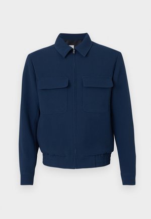 Veste zippée bleu marine avec col, manches longues, deux poches à rabat sur la poitrine et taille élastiquée sur un fond uni.
