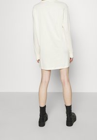 Abito a maniche lunghe color crema con vestibilità rilassata, scollo rotondo e orlo dritto. Indossato con stivaletti neri con suola spessa.