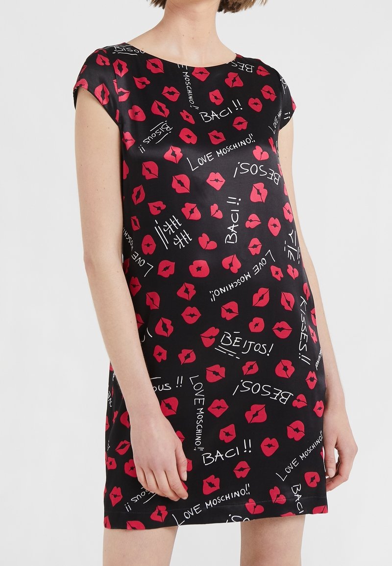 Robe noire à manches courtes avec des imprimés de lèvres rouges et des mots blancs comme "Love Moschino," "Baci," et "Besos" dispersés partout.