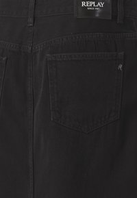 Bakvy av svarta denimjeans som visar en enda bakficka och en svart Replay-märkesetikett med vit text.