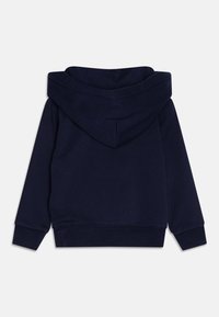 Námořnická modrá mikina s prostornou kapucí, žebrovanými manžetami a spodním lemem. Tkanina se zdá být hladká a jemná, s jednoduchým, jednobarevným designem.