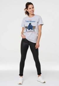 Gray cotton t-shirt featuring Cookie Monster graphic, paired with black leggings and white sneakers. T-shirt has short sleeves and a relaxed fit.