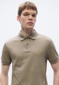 Polo bege com gola clássica, pala com dois botões e mangas curtas. Apresenta um discreto logótipo "BOSS" no peito. Textura lisa.