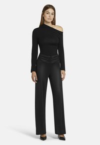 Zwarte one-shoulder bodysuit met lange mouwen, gecombineerd met high-waisted, loose-fit broeken. Soepele stof en geplooide details in de taille.