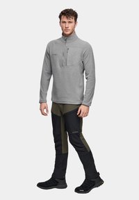 Szary polar z pół zamkiem i kieszenią na piersi, zestawiony z czarnymi i oliwkowymi spodniami cargo z kieszeniami i wzmocnionymi panelami.