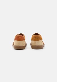 Scarpe in suede beige e arancione con una suola in gomma marrone liscia, caratterizzate da un design arrotondato e un logo Camper impressato sul tallone.