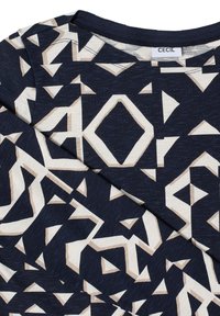 Granatowy materiał z beżowymi i białymi geometrycznymi kształtami, ukazujący złożony rękaw i dekolt z metką odzieżową "CECIL."