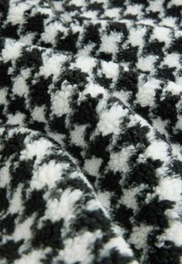Material de țesătură cu un model alb-negru de houndstooth, cu o suprafață moale și texturată, având o apariție pufoasă și blănoasă.
