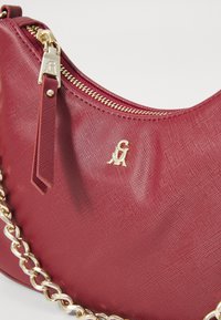 Maroon handbag with textured finish, gold hardware, and a zip closure. Features a decorative gold chain strap and embossed logo.