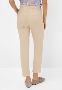 Beige Hosen mit einer schmalen Passform, die über Gesäßtaschen und eine weiche Textur verfügen. Tragen sie mit einfachen braunen Ballerinas, die knapp über dem Knöchel enden.