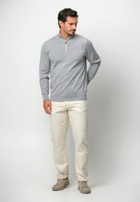 Grau pullover mit einem halben Reißverschluss-Kragen, gerippten Bündchen und Saum, kombiniert mit elfenbeinfarbenen Hosen und hellgrauen Turnschuhen.