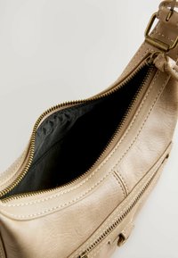 Borsa a mano in pelle beige con finitura testurizzata, chiusura con zip e fodera in tessuto nero. Caratterizzata da hardware dorato e cuciture a contrasto.