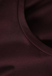 Bordowa tkanina o gładkiej fakturze i okrągłym dekolcie. Materiał wydaje się miękki i lekko połyskujący, prezentując jednolity kolor.