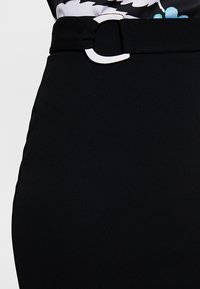 Černá sukně s hladkou texturou, vybavená širokým pásem se stříbrnou kulatou sponou, střižená na míru a s jemnými švovými detaily.