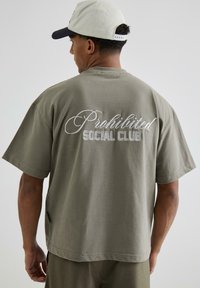 Tricou din bumbac verde măsliniu cu mâneci scurte, având brodat pe spate textul alb "Club Social Interzis". Etichetă vizibilă pe marginea laterală.