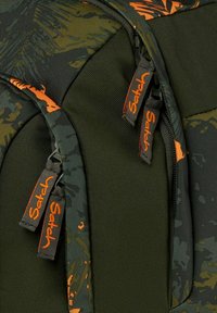 Sac à dos camo vert et orange avec un tissu durable, des fermetures éclair texturées avec des étiquettes de logo, et un design structuré pour un usage pratique.
