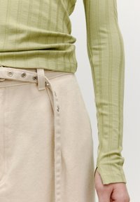 Langsleeve, lichtgroen top met verticale strepen, gecombineerd met beige broek met een zijsluiting met knopen en een gestructureerde stof.