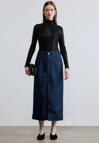 Μαύρο εφαρμοστό τοπ με ζιβάγκο και υφασμένο μοτίβο, συνδυασμένο με φούστα από σκούρο τζιν μεσαίου μήκους, με μπροστινό άνοιγμα και ραμμένες λεπτομέρειες.