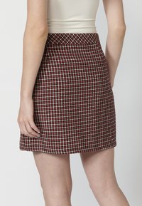 Jupe mini à carreaux rouge et blanc avec un design structuré, dotée d'une taille et d'un ourlet lisses, fabriquée dans un tissu texturé.