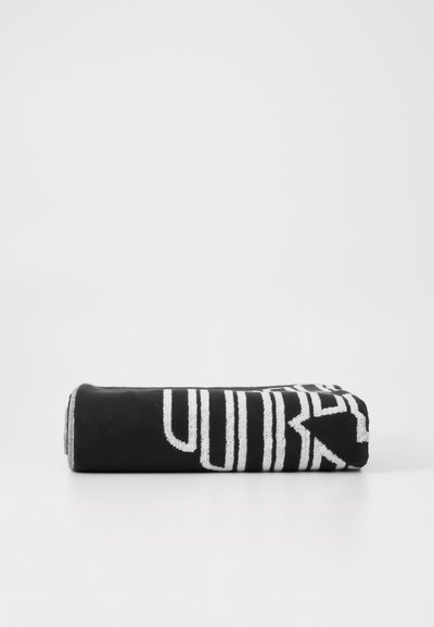 Black towel rolled up, featuring bold white text design. Soft texture with contrasting colors, emphasizing modern graphic pattern.