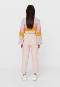 Flerfärgad stickad tröja med rosa, gul och lila ränder; mjuk textur. Kombinerad med ljusrosa byxor och vita sneakers.