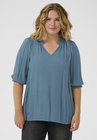 Blue, lightweight blouse with a V-neckline, pleated detailing, and semi-batwing sleeves. Features a smooth texture and relaxed fit.