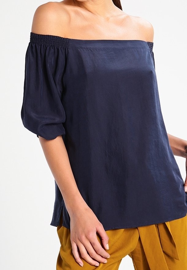Navy off-the-shoulder blouse with elastic smocking at the neckline, short puff sleeves, and a relaxed fit. Smooth, lightweight fabric.