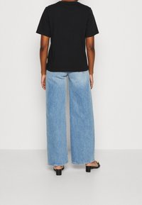Camiseta de algodón negra con mangas cortas, combinada con jeans de mezclilla de pierna ancha en un tono azul claro, con dobladillo sin terminar y un ligero desvanecimiento. Sandalias negras de tacón bloque.