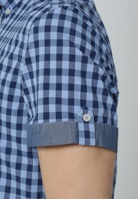 Chemise à manches courtes à carreaux bleu et marine avec poignets à accents en denim, dotée d'une fermeture à boutons au niveau du poignet et d'un col structuré.