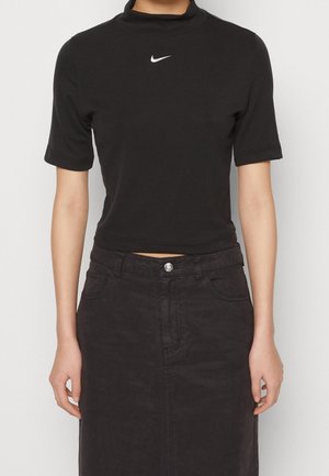 Black cropped t-shirt with a high collar and short sleeves, featuring a small white Nike logo on the front, paired with a dark skirt.