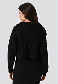Maglione nero a maglia con texture a coste, design cropped, colletto ampio e maniche lunghe. La parte posteriore presenta un dettaglio a coste orizzontali.