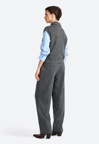 Gilet à carreaux gris associé à une chemise bleu clair et un pantalon large gris. La tenue présente un tissu texturé et des éléments de design ajustés.