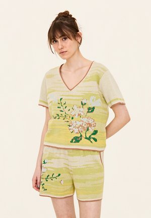 Breien loungewear set met een gele V-hals top met bloemenpatronen en bijpassende shorts. Gevoed materiaal met een subtiel gestreept patroon.