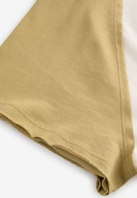 Cotton t-shirt featuring a curved hem, split design in khaki and white colors, with smooth texture and visible stitching details.