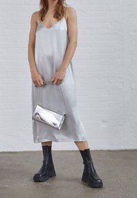 Robe nuisette en soie argentée avec un décolleté en V, associée à des bottes noires à semelles épaisses et une pochette métallique argentée brillante avec une bandoulière en chaîne.