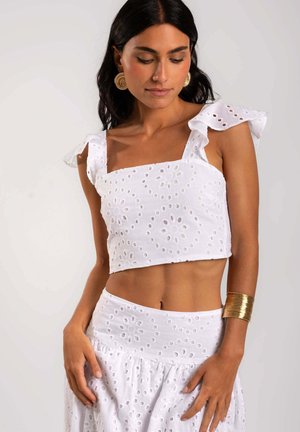 Top corto blanco con un patrón de ojo de perdiz floral, escote cuadrado y tirantes con volantes, combinado con una falda a juego que presenta un detalle similar.